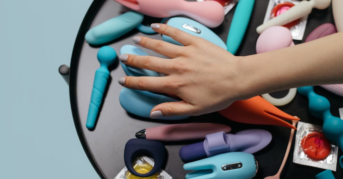 The Nightstand shop A hand reaching over a variety of colorful sex toys arranged on a table.